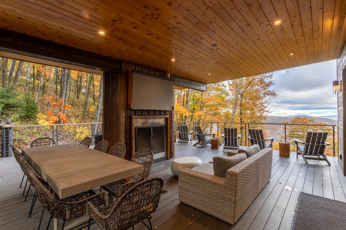 A covered outdoor deck features a dining table, fireplace, and comfortable seating, all oriented to take in the surrounding mountain vistas and autumn foliage. The warm glow of the fire and the tranquil setting evoke relaxation and sociability, matching the section's invitation to host dinners or cozy up under the stars.