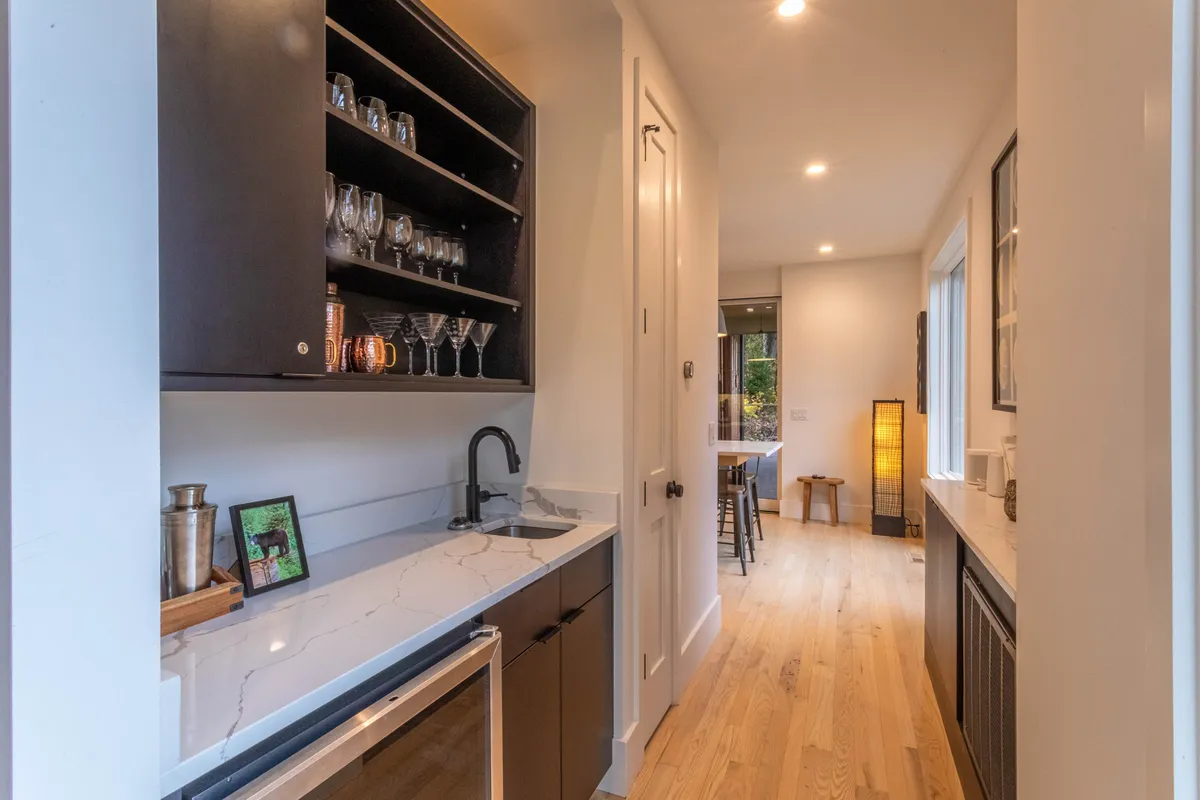 A chic bar area with elegant glassware, a marble countertop, and wooden accents. The scene is set for entertaining, inviting guests to mix drinks and enjoy each other's company in a stylish, welcoming corner of the lodge.