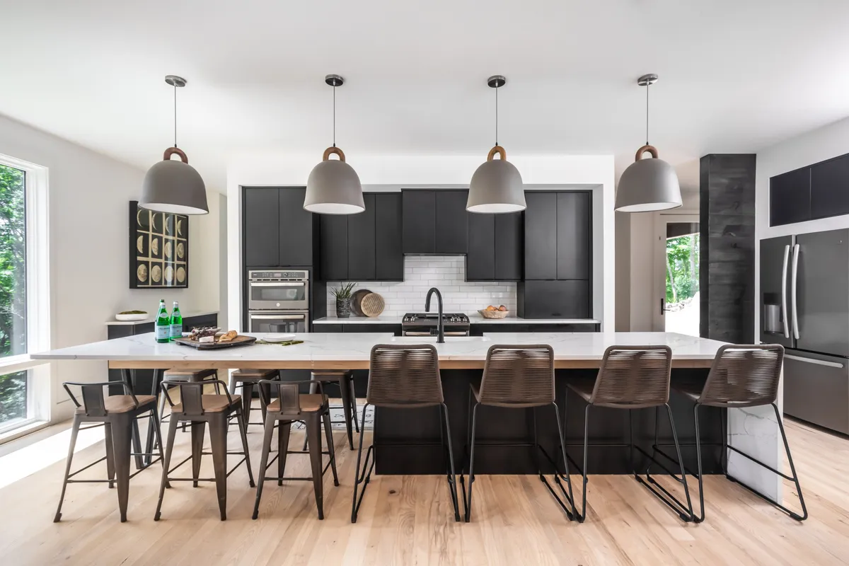 A spacious, contemporary kitchen featuring a large island countertop with comfortable stools, chic pendant lighting, and stylish cabinetry. The layout invites group cooking and socializing, evoking the feel of gourmet gatherings and shared culinary adventures.