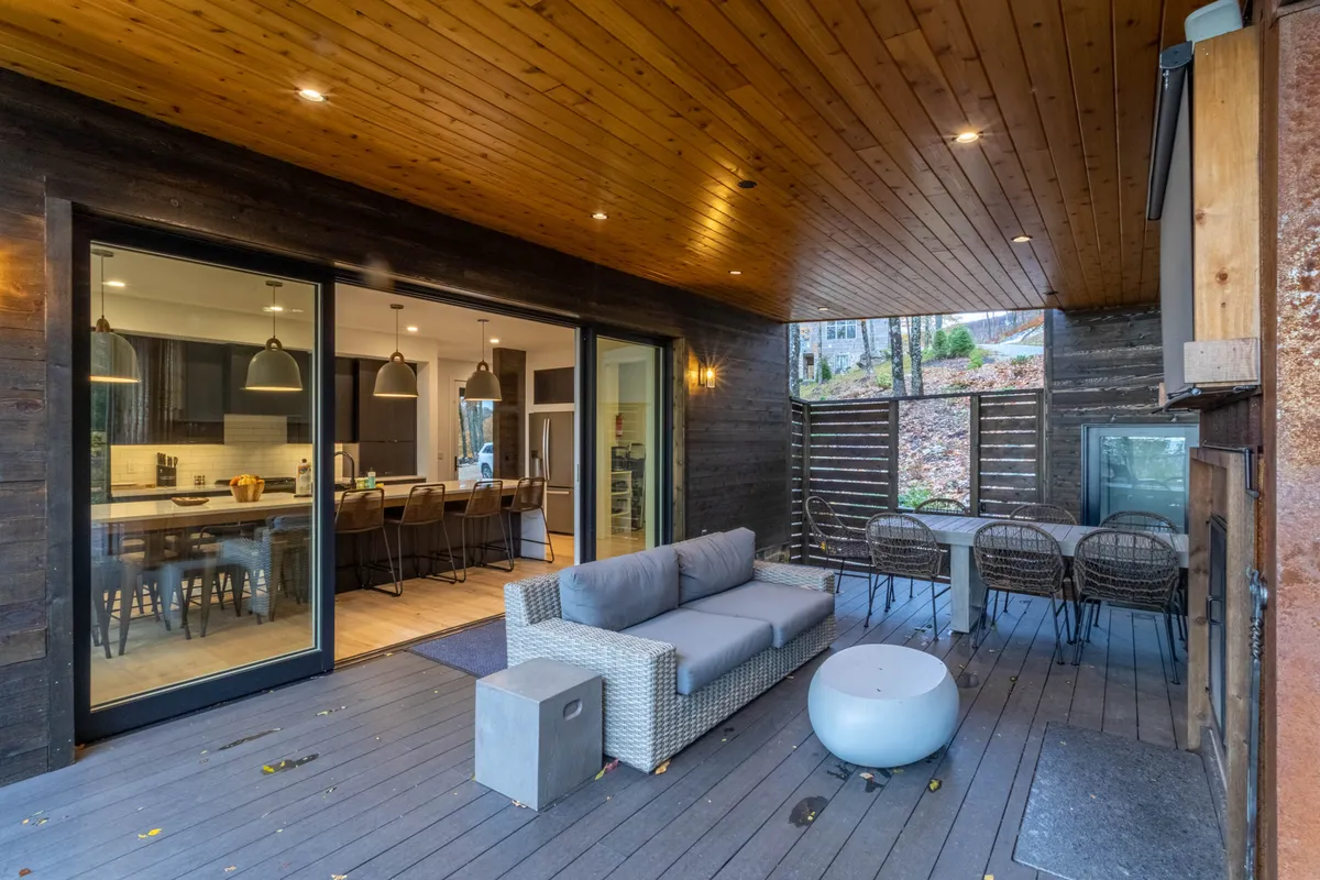 This image captures a comfortable outdoor seating area and dining table positioned directly beside large glass pocket doors that open into the interior living space. The seamless connection between the indoors and outdoors is highlighted, and the view suggests a setting perfect for both relaxation and entertaining against a scenic backdrop.