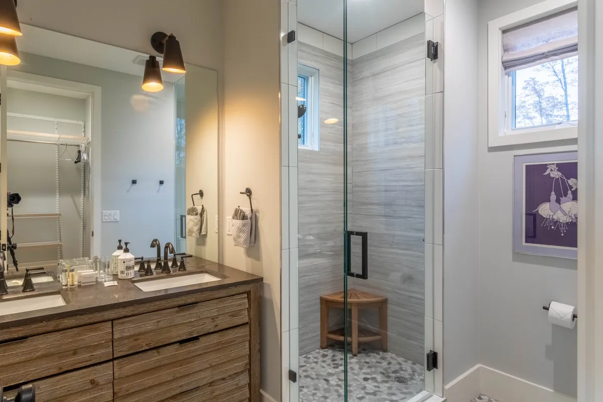 A bright, modern bathroom with a double sink vanity, a glass shower enclosure, and decorative wall art. The mood is calm and refreshing, reminiscent of a spa experience.