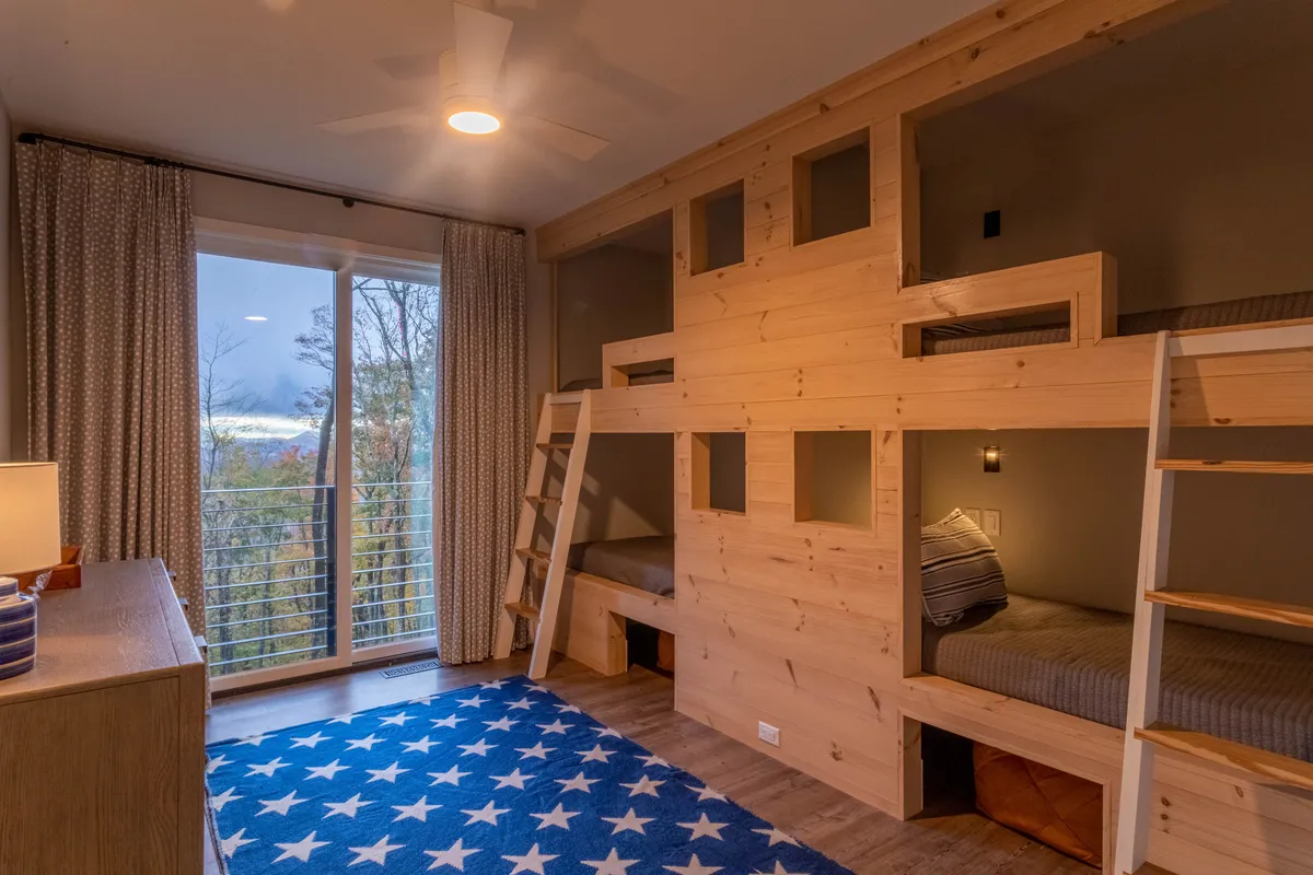 A playful bunk room with built-in bunk beds, a cheerful rug, and a window allowing for natural light. The mood is playful and cozy, ideal for children or teens to relax and play.